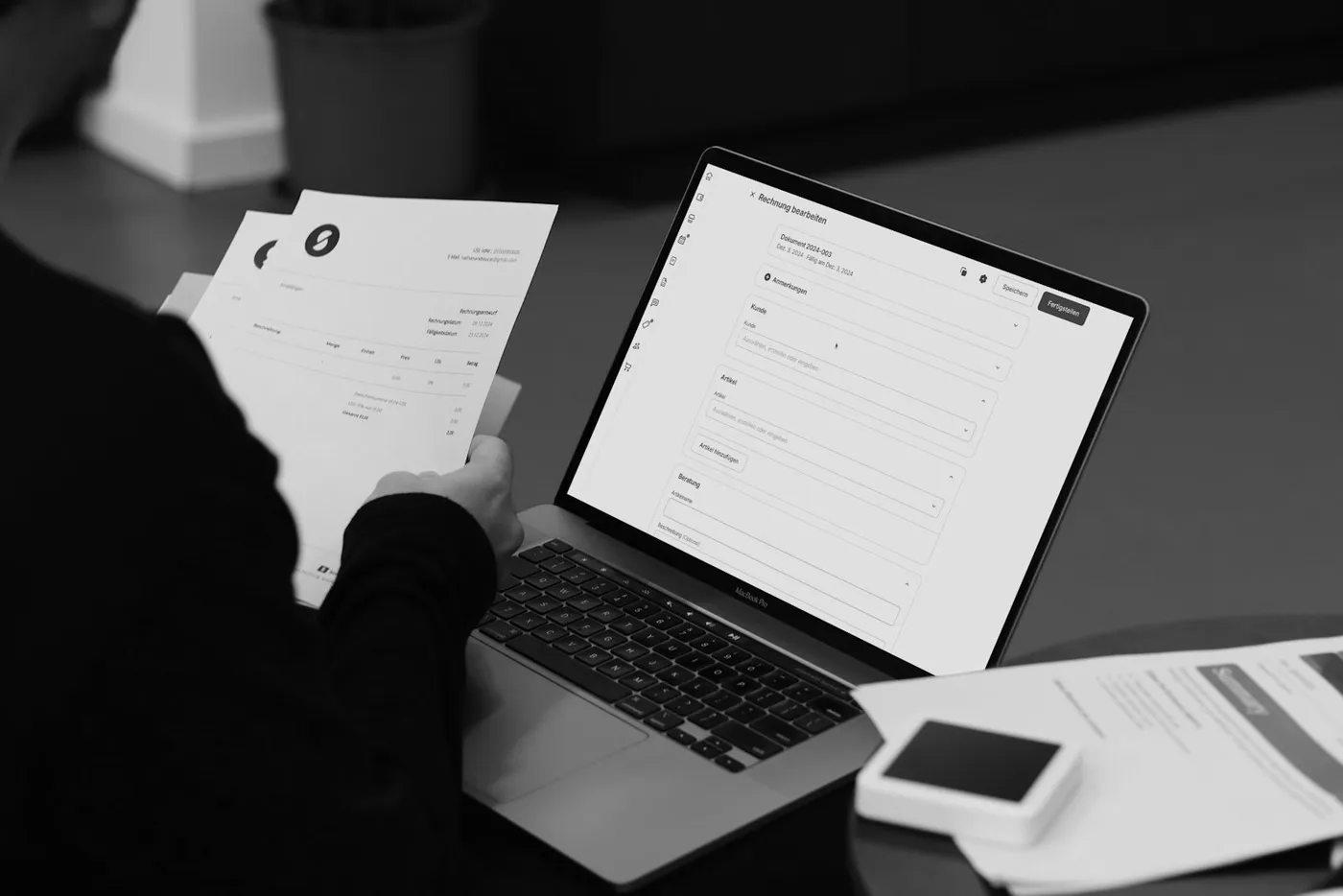 A person reviewing a printed invoice beside a laptop showing a billing screen